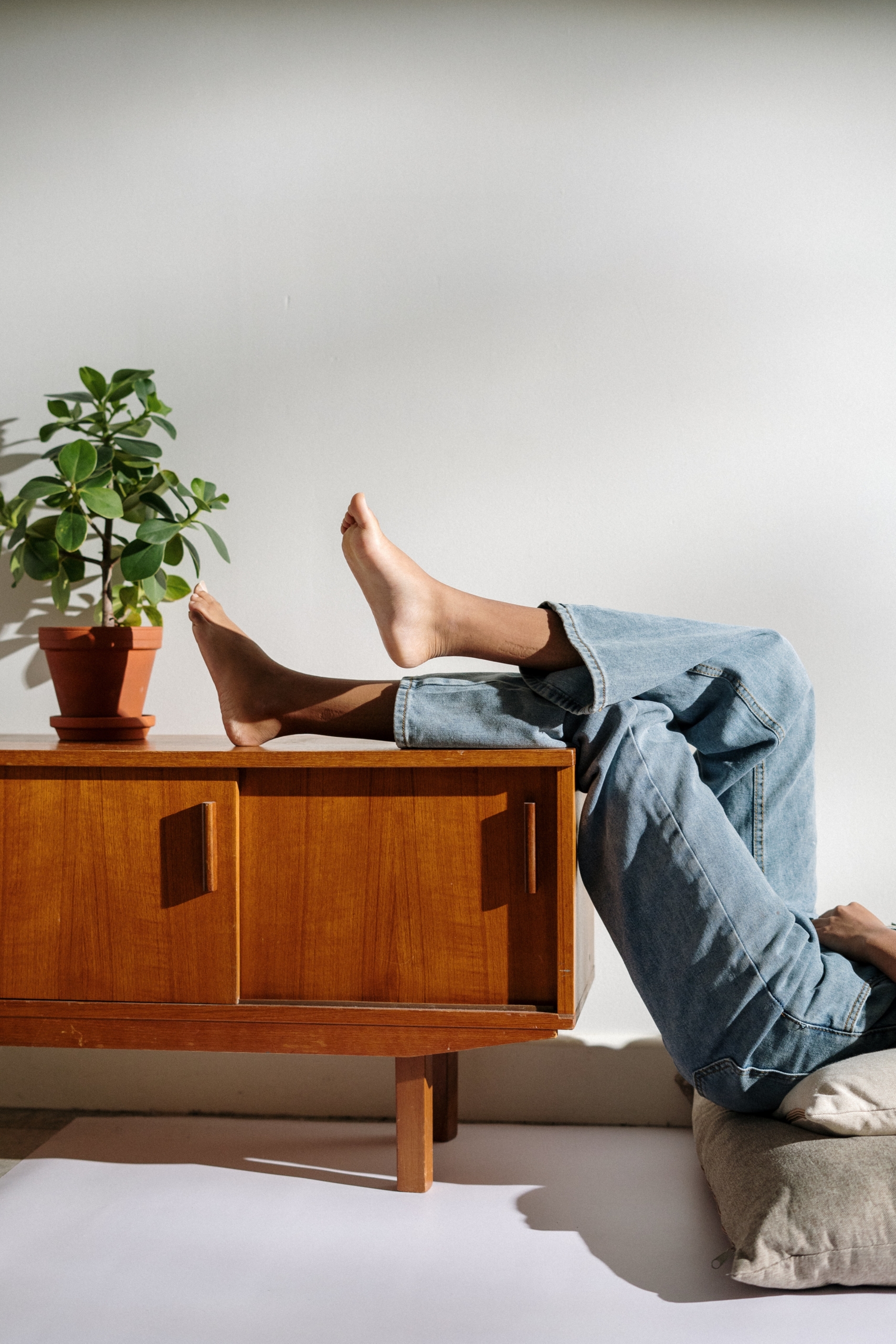 Mueble aparador de madera con planta y piernas de una persona apoyadas en el